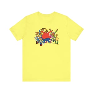 May include: A yellow t-shirt featuring a cartoon image of a group of people dancing. The people are all wearing different coloured clothes and have different hairstyles. The image is centred on the shirt.