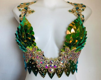 May include: A green and gold sequined bra top with iridescent accents. The bra top has a plunging neckline and a scalloped bottom edge.