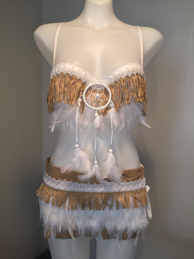 May include: A two-piece costume with a Native American theme. The top features a white lace trim, tan fringe, and a dreamcatcher. The bottom has a tan belt with white lace and fringe, and white feathers.