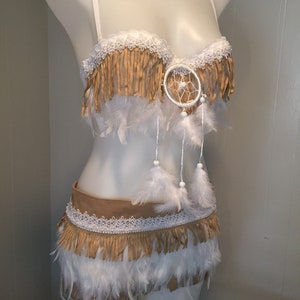 May include: A two-piece costume set on a mannequin. The top is a bra with fringe and a dreamcatcher. The bottom is a skirt with fringe and feathers. The colors are tan, white, and cream.