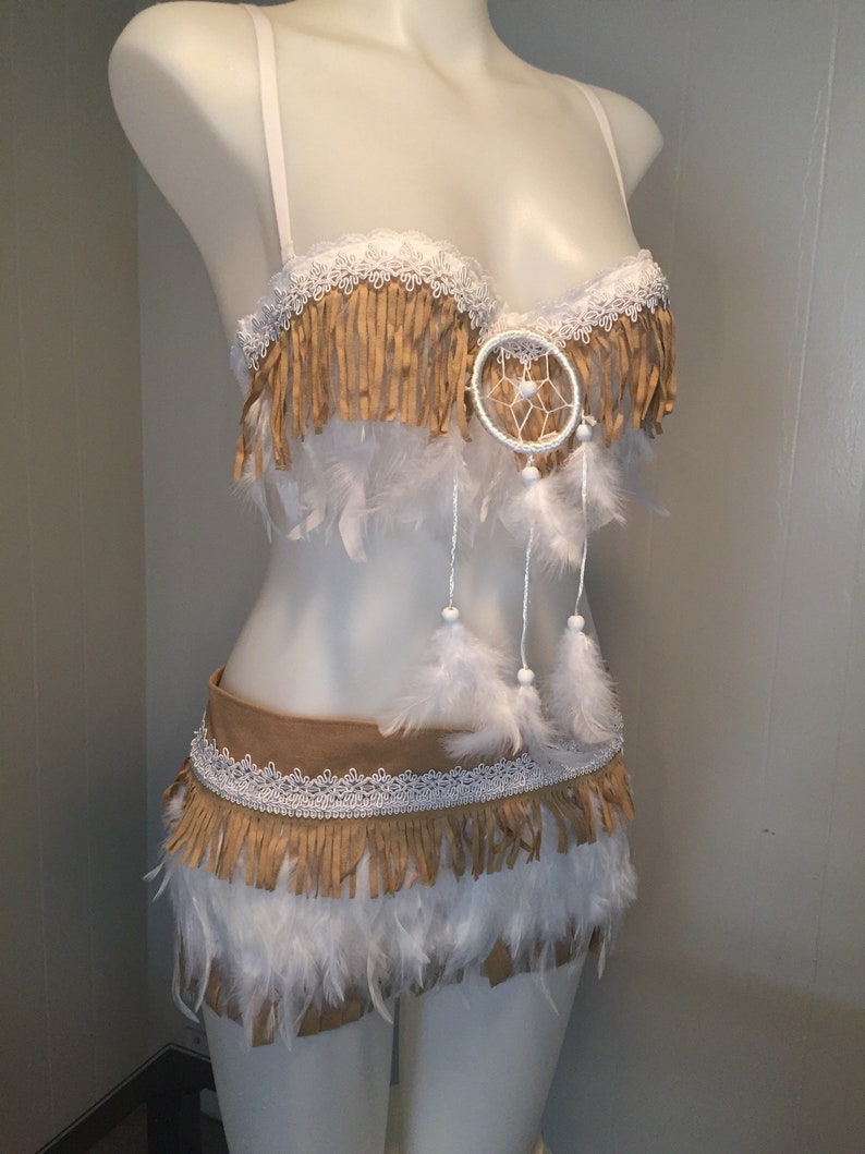 May include: A two-piece costume set on a mannequin. The top is a bra with fringe and a dreamcatcher. The bottom is a skirt with fringe and feathers. The colors are tan, white, and cream.