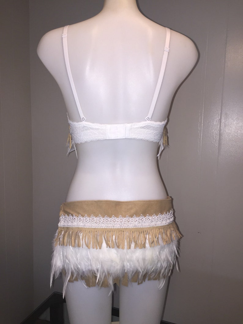 May include: A white lace bra and a matching skirt with a tan suede waistband, white lace trim, and tan fringe. The skirt has a layer of white feathers at the bottom. The outfit is displayed on a white mannequin.