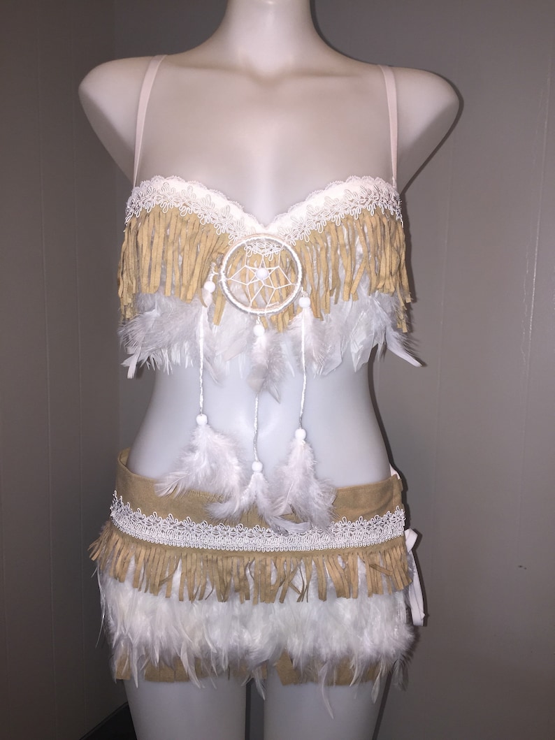 May include: A two-piece costume set on a mannequin. The top is a bra with fringe and a dreamcatcher. The bottom is a skirt with fringe and feathers. The costume is tan, white, and cream-colored.