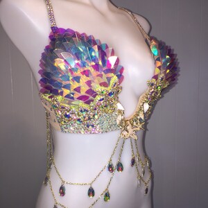 May include: A iridescent, multi-colored, sequined bra with a gold chain and crystal accents. The bra has a low-cut neckline and is decorated with a starfish.