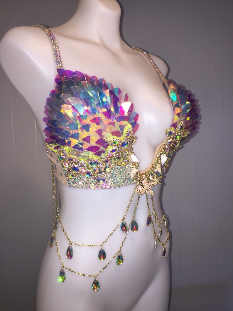 May include: A iridescent, multi-colored, sequined bra with a gold chain and crystal accents. The bra has a low-cut neckline and is decorated with a starfish.