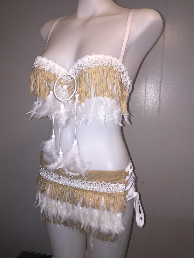 May include: A two-piece cream-colored lingerie set with a Native American theme. The top and bottom feature tan fringe, white lace, and white feathers. A dreamcatcher is centered on the top. The set is displayed on a mannequin.