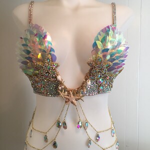 May include: A iridescent mermaid-themed bra top with a gold chain and crystal accents. The bra top features a seashell and starfish design.