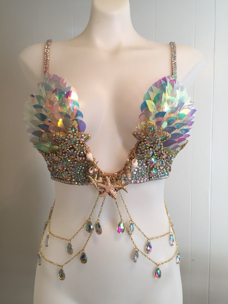 May include: A iridescent mermaid-themed bra top with a gold chain and crystal accents. The bra top features a seashell and starfish design.