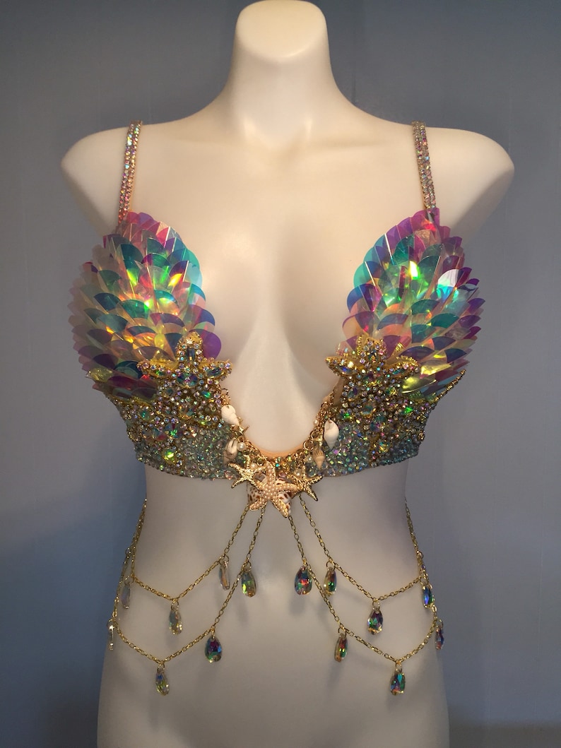 May include: A mermaid-themed bra top with iridescent sequins, gold chains, and crystal accents. The bra top features a seashell design and a starfish pendant.