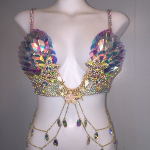 May include: A iridescent gold and white bra with a seashell and starfish design. The bra has a chain with iridescent teardrop crystals hanging from it.