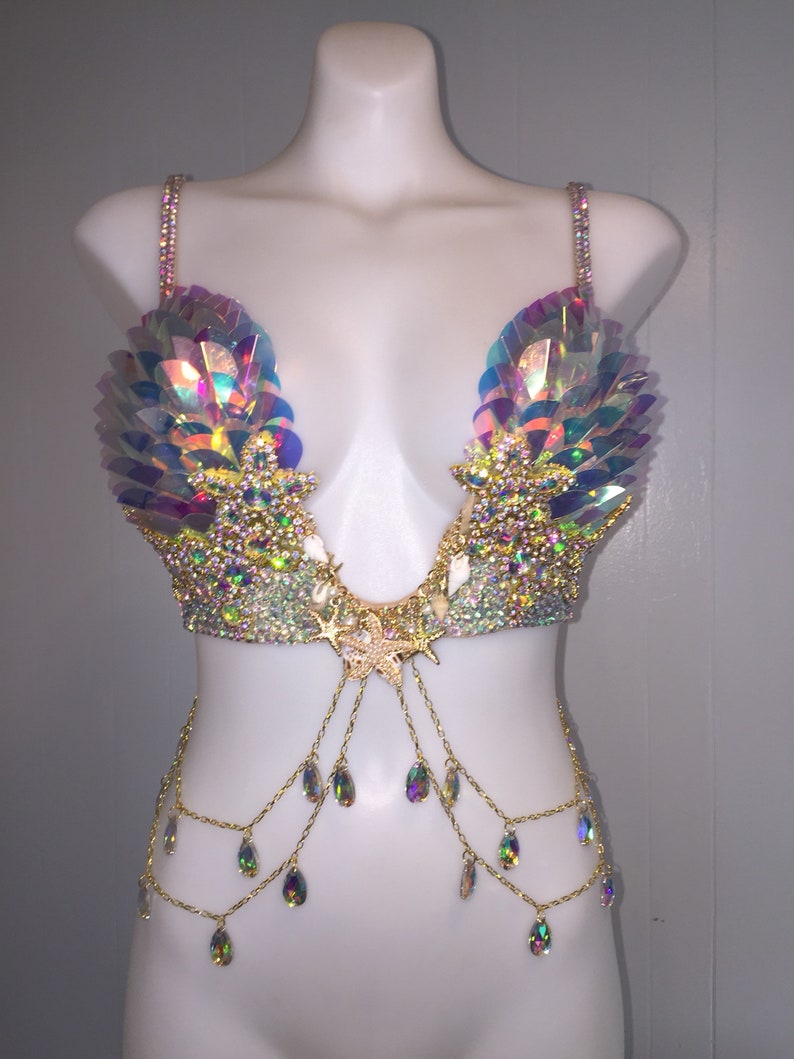 May include: A iridescent gold and white bra with a seashell and starfish design. The bra has a chain with iridescent teardrop crystals hanging from it.