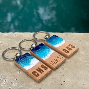 May include: Three wooden keychains with blue and white resin ocean wave designs. The keychains are engraved with "CHS", "10.9.11", and "843".