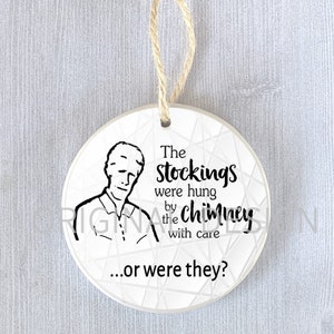 Op de afbeelding: Witte kerstbal van keramiek met een zwart-witte illustratie van een man en de tekst "The stockings were hung by the chimney with care...or were they?"