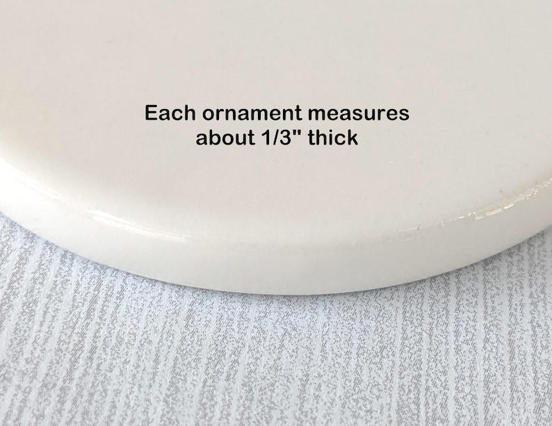 Op de afbeelding: Close-up van een wit keramiek ornament, met de rand zichtbaar. Elk ornament is ongeveer 1/3 inch dik.