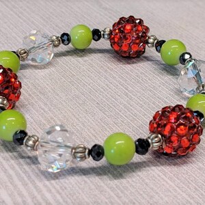May include: A red and green beaded bracelet with clear crystal beads and silver accents. The bracelet features red rhinestone balls and green glass beads.