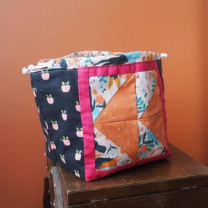 Peut inclure: Un sac de rangement en tissu rose et noir avec un motif patchwork. Le sac a une fermeture à cordon et est fait de tissu de coton.