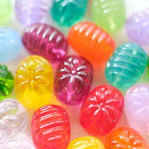 May include: A collection of colorful, translucent, oval-shaped candies. The candies are in various colors, including red, orange, yellow, green, purple, and blue. Some candies have a ribbed texture, while others have a flower-like design.