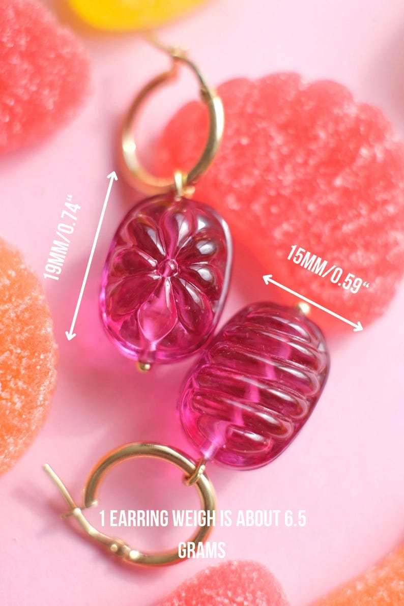 May include: A pair of pink, gold-toned earrings. The earrings are 19mm/0.74" and 15mm/0.59" in size, with a weight of about 6.5 grams each. The earrings have a gold hoop and a pink, oval-shaped, transparent charm.