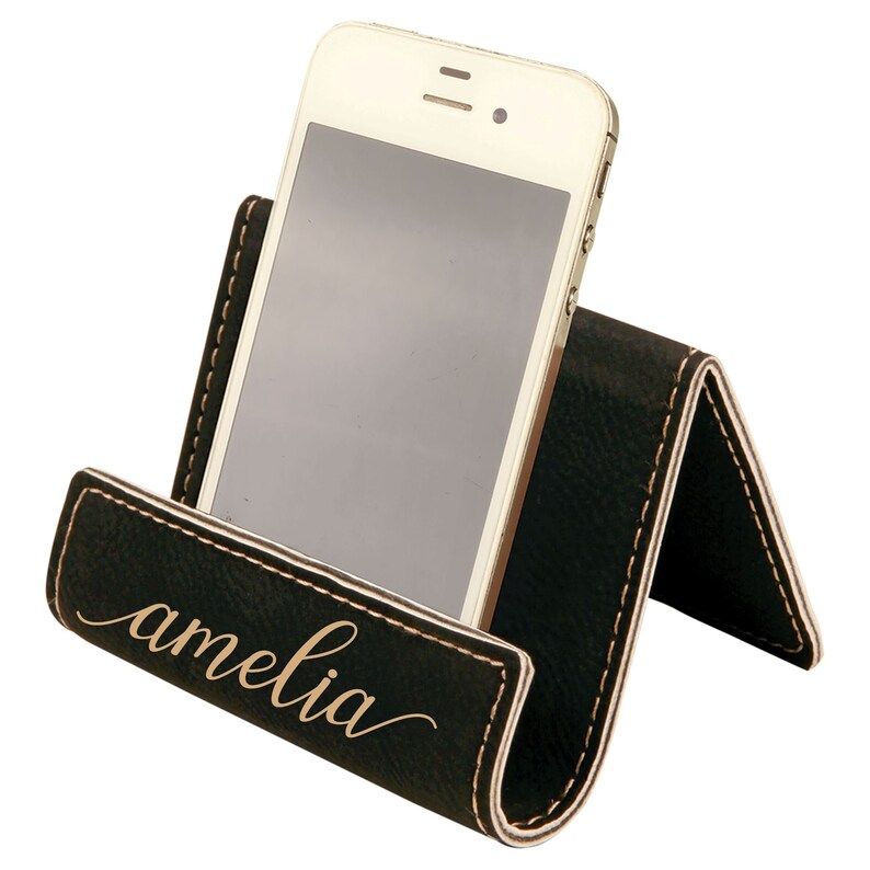 May include: Black leather phone stand with a gold inscription that reads "amelia".