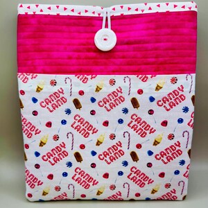 May include: A quilted fabric sleeve with a white button closure. The top section is hot pink, and the bottom section is white with a repeating pattern of ice cream, candy canes, and the words "Candy Land" in red.