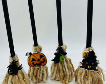 May include: Four miniature broomsticks with Halloween-themed decorations. The broomsticks are made of brown yarn and have black sticks. The decorations include a pumpkin, a witch, and a haunted house.