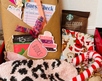 May include: A red gift box filled with various items, including a brown paper envelope with a handwritten "Guest Check" and "DING LIST" note, a pink and brown fuzzy sock, a red and white candy cane, a small brown bag with the text "Touch Organic" and a heart-shaped sticker that says "BOOKS", a small brown bag with a stack of books, a small white and red patterned fabric with a Santa Claus design, and a brown packet of hot cocoa mix with the text "HOT COCOA" and "DOUBLE CHOCOLATE".