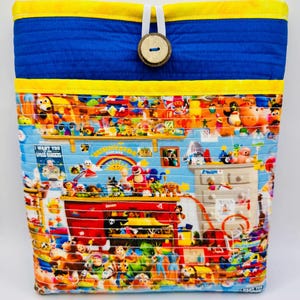 May include: A quilted fabric pouch featuring a vibrant print of various cartoon characters and toys from the Sunnyside Daycare setting. The top section is solid blue with yellow trim, secured by a white elastic loop and a round wooden button.
