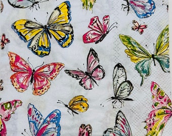 May include: White paper napkin with a repeating pattern of colorful butterflies. The butterflies are in various sizes and feature a range of colors, including yellow, pink, blue, and green. The napkin has a textured surface.