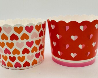 May include: Two red and white heart patterned cupcake liners. The liners have a scalloped edge and are made of paper.