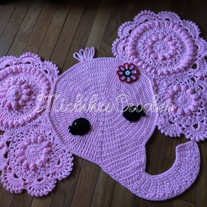 May include: A pink crocheted elephant rug with a matching set of two circular doilies. The elephant has black eyes, a flower, and the text "Michikos Crochet". The rug is made of soft yarn and is suitable for a nursery or children's room.