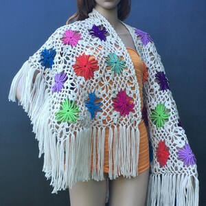 May include: White crochet shawl with colorful flower accents and fringe.