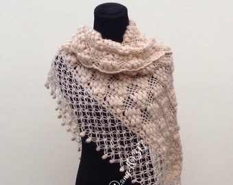 May include: A beige crocheted shawl with a textured pattern and a fringe border. The shawl is draped over a black mannequin.