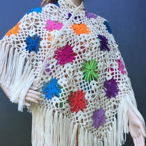 May include: A white crochet poncho with colorful flower accents and fringe.