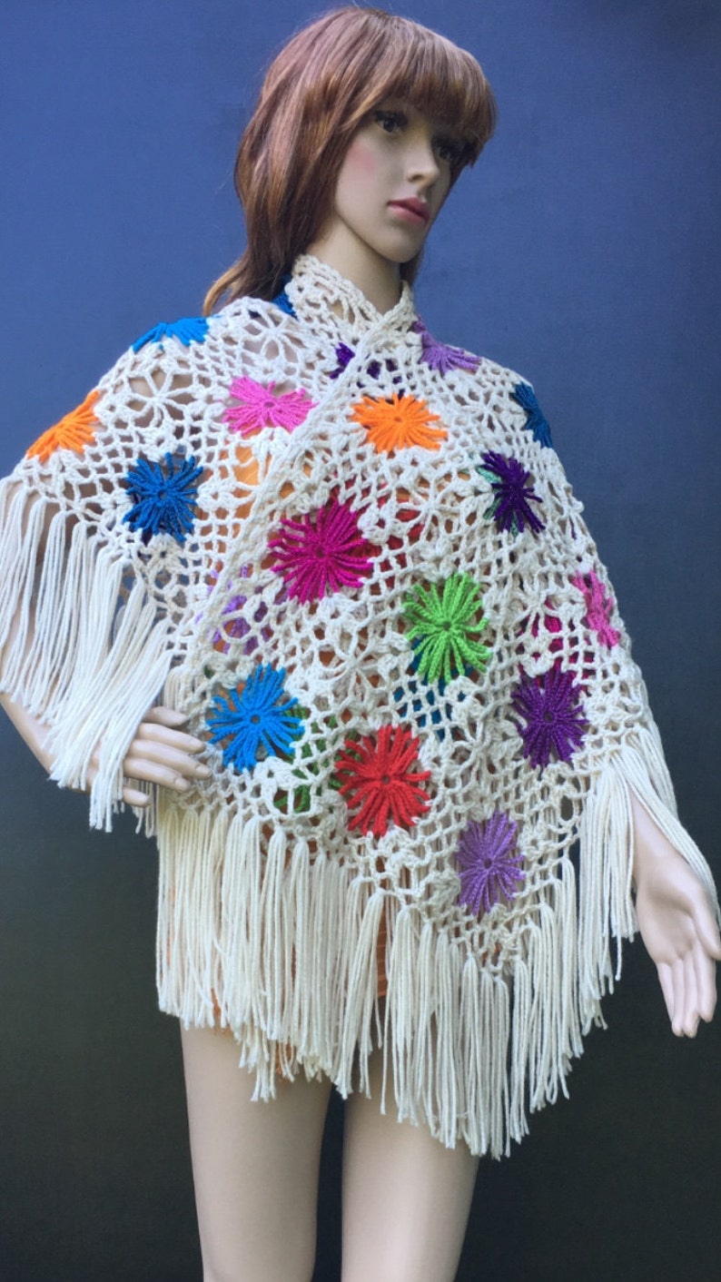May include: A white crochet poncho with colorful flower accents and fringe.