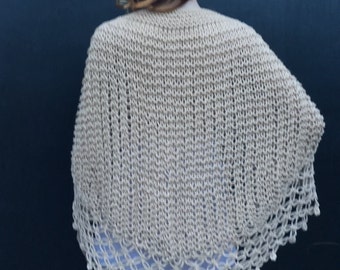 May include: A beige knitted shawl with a crocheted border. The shawl is draped over a person's shoulders.
