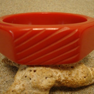 Op de afbeelding: Een rode plastic armband met een diagonaal gestreept patroon.