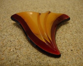 May include: A vintage brooch made of red, yellow, and black plastic. The brooch is shaped like a stylized leaf with a curved, pointed tip.