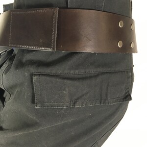 May include: Black cargo trousers with a brown leather belt featuring metal accents. The belt has a buckle and four metal rivets.