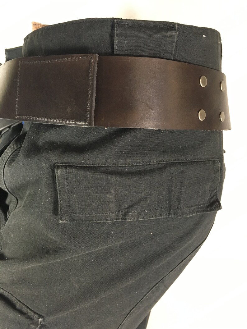 May include: Black cargo trousers with a brown leather belt featuring metal accents. The belt has a buckle and four metal rivets.