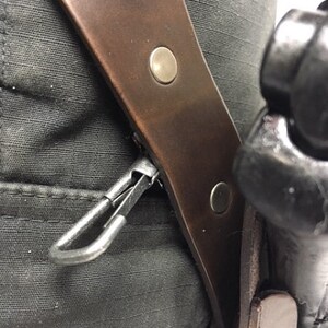 May include: A brown leather holster with a metal clip and two metal poppers. The holster is attached to a black belt.
