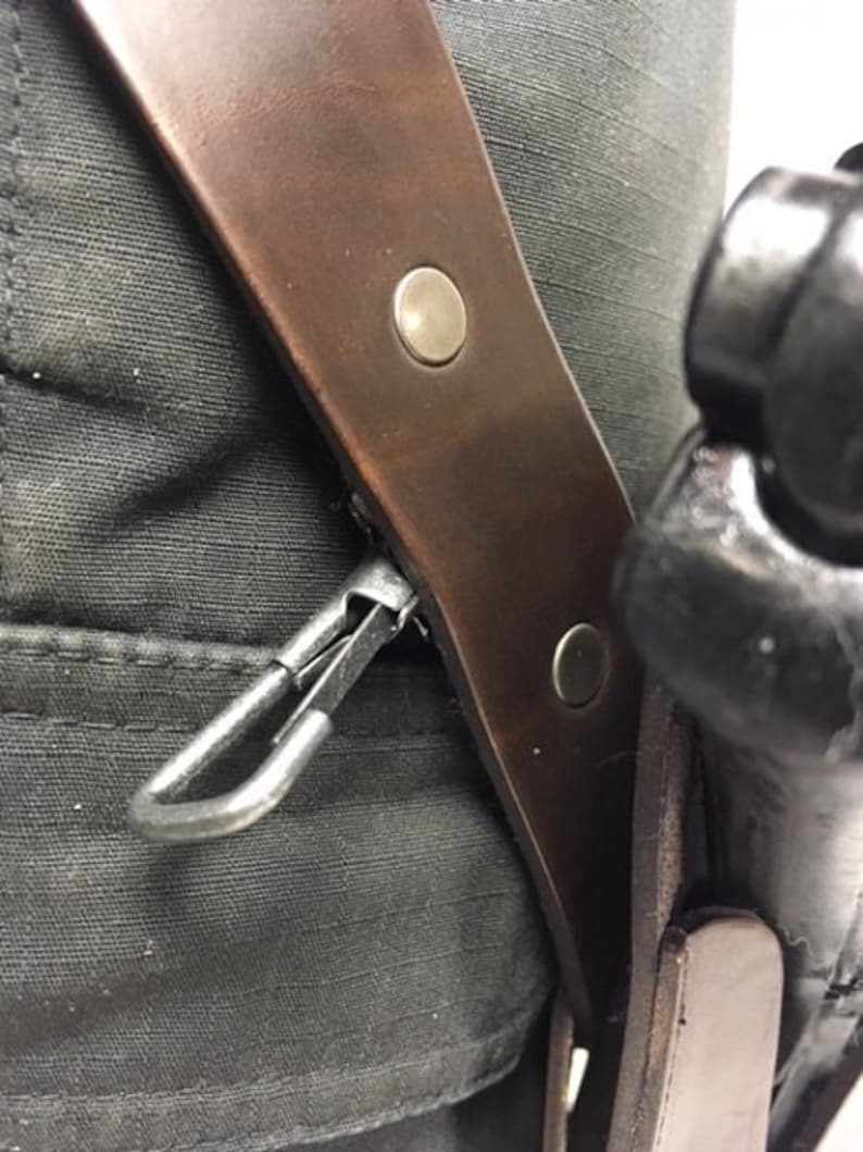 May include: A brown leather holster with a metal clip and two metal poppers. The holster is attached to a black belt.
