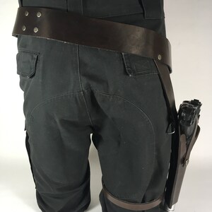 May include: Black cargo trousers with a brown leather belt and a brown leather holster with a black gun attached.