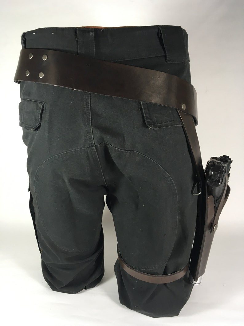 May include: Black cargo trousers with a brown leather belt and a brown leather holster with a black gun attached.