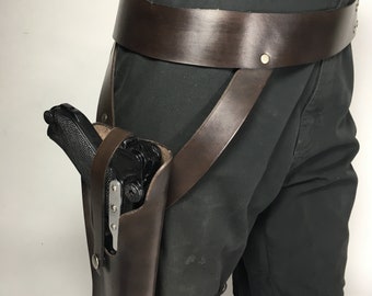 May include: A brown leather thigh holster with a black gun inside. The holster is attached to a brown leather belt with straps that go around the leg.