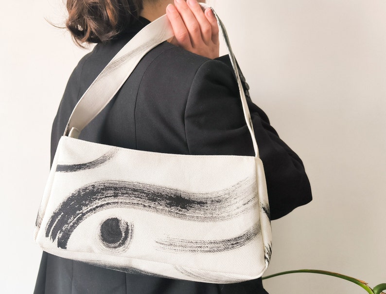 Baguette bag with hand painted abstract picture is an unique accessory for everyday use and was made from upcycled materials. The bag has a lining with a beautiful print and zipper. The bad is in a basic black and white colours.