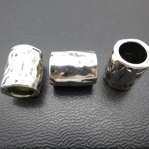 Op de afbeelding: Drie zilveren metalen kralen met een getextureerd oppervlak. De kralen zijn cilindrisch van vorm en hebben een gat in het midden.