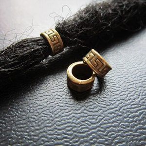 May include: Three gold-colored metal beads with a geometric pattern. The beads are designed to be used as hair ties or hair accessories.