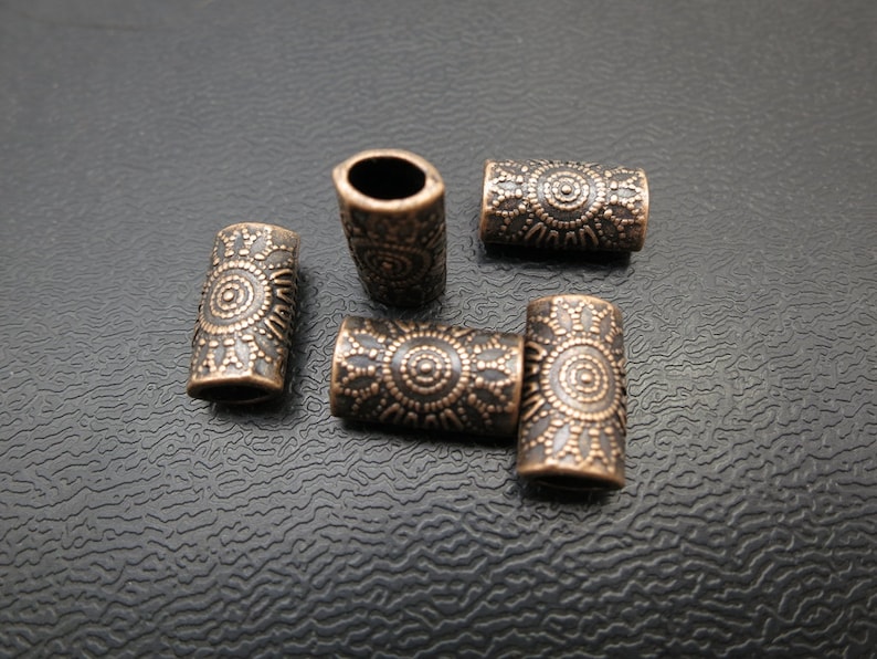 May include: Five antique gold-toned metal beads with a circular pattern. The beads are about 1 inch long and have a slightly rounded shape.