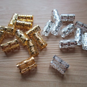 May include: A collection of gold and silver metal hair beads. The beads are cylindrical and have a decorative, openwork design.