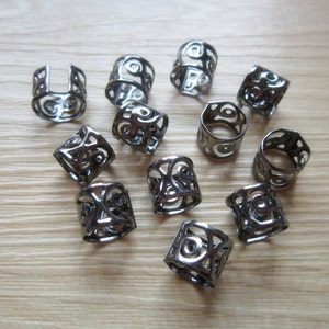 May include: A set of 12 black metal hair rings with intricate designs. The rings are all the same size and shape, and they have a slightly textured finish.
